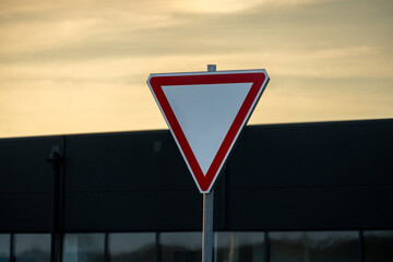 A yield sign is prominently displayed with a colorful evening sky behind it. The urban setting features a dark building casting shadows as the day ends