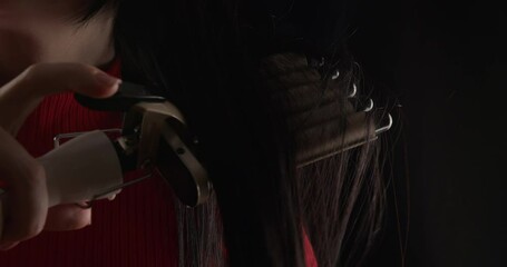 Woman curling wavy curls with triple curling iron, demonstration of professional hair stylist attribute in action on black background