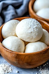 Fototapeta premium Fresh raw dough balls dusted with flour in wooden bowl on dark background, close up view of homemade bread or pizza preparation process.