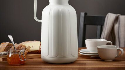 Closeup of a jug, honey jar, food and cups on a table.
