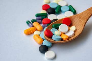 Close up of colorful pills or capsules on wooden spoon with customizable space for text. Medical and health matters concept.