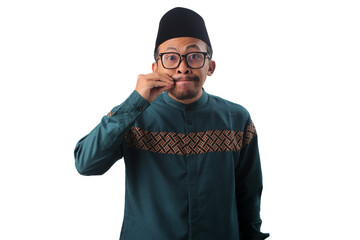 Asian Muslim man making a zip gesture with his fingers over his mouth, symbolizing silence,...