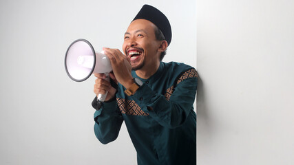 Asian Muslim man holding a megaphone while peeking from behind a wall, showing an excited 