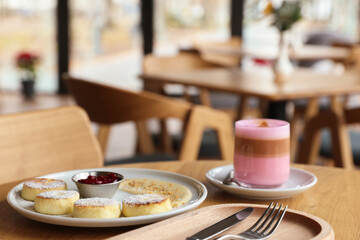 Delicious cottage cheese pancakes and pink latte served on wooden table indoors