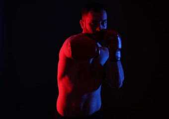 Man in boxing gloves fighting on black background in neon lights