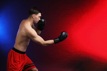 Man with boxing gloves fighting on dark background in neon lights, space for text