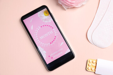 Smartphone with period calendar application, menstrual products and flower on beige background,...