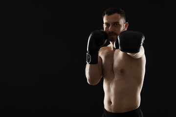 Man in boxing gloves fighting on black background, space for text