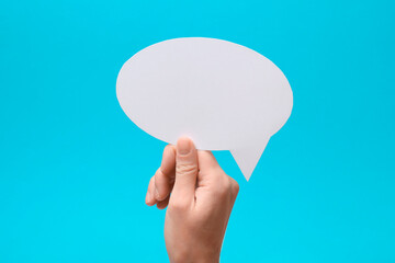 Woman holding blank speech bubble on light blue background, closeup. Space for text
