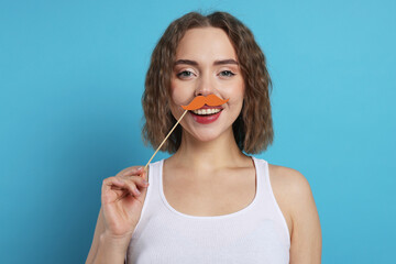 Smiling woman with fake paper mustache on light blue background