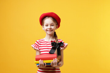 Schoolgirl with beret and books on yellow background
