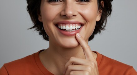 Close-up of a Smiling Woman with Perfect Teeth, Touching her Chin, Wearing a Rust-Colored T-Shirt Against a Gray Background