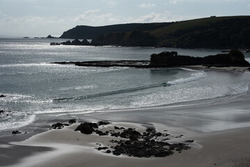 Backlit, and silhouetted headlands jutting out into the Pacific Ocean at Tawharanui Regional Park, Auckland, New Zealand. Anchor Bay beach in the foreground.