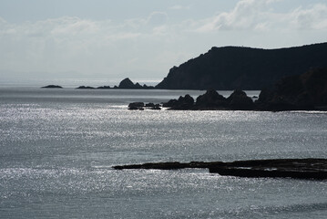 Backlit, and silhouetted headlands jutting out into the Pacific Ocean at Tawharanui Regional Park, Auckland, New Zealand.