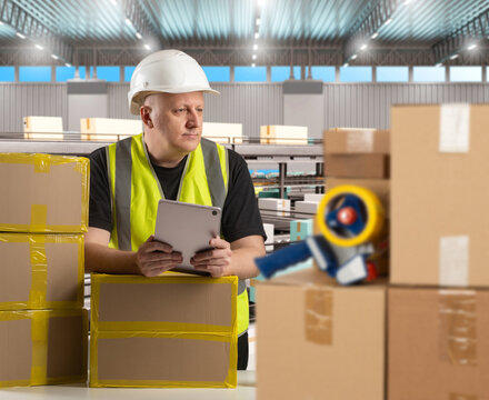 Man factory worker with conveyor belt. Boxes and tape near factory employee. Man near conveyor belt in production hangar. Packaging line at manufacturing plant. Packer guy holds tablet computer
