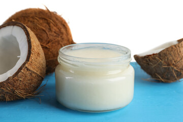 Coconuts and cooking oil on light blue wooden table against white background