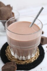 Tasty chocolate milk in glass and pieces of chocolate on white wooden table, closeup