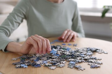 Woman solving puzzle at wooden table indoors, closeup