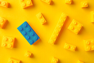 Difference, uniqueness, individuality. Blue building block among yellow ones on color background, top view