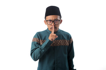 Asian Muslim man making a quiet gesture with his finger on lips, symbolizing secrecy or silence. Taboo topic, censorship, or confidential talk concept during ramadan. Isolated on a white background
