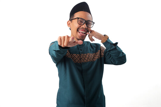 Smiling Asian Muslim man standing while making a "call me" hand gesture and pointing directly at the camera, expressing friendliness and approachability. Isolated on a white background