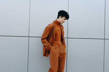 Stylish young man in an orange outfit against a grey minimalist wall He gazes downward, exuding a...