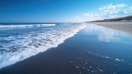 Gently lapping the shore of a sandy beach under a clear blue sky, soft waves create a serene and peaceful scene, offering a tranquil escape.
