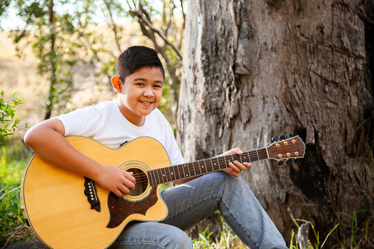 Boy playing country music on acoustic guitar in bushland
