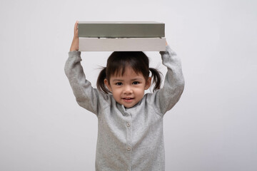 A cheerful child playfully holds a box above her head, showcasing innocence and joy. An engaging...