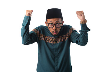 Surprised Asian Muslim man clenching fists in a winner gesture, celebrating success and joy during Eid al-Fitr. Expressing excitement, triumph, and gratitude after completing Ramadan fasting