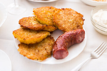 Potato pancakes with fried sausage on white plate