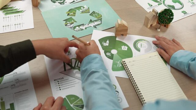 Excellent business people discuss about eco house project on messy table with green energy graph usage choose or analyze alternative power, decrease carbon to save earth. Focus on hand. Delineation.