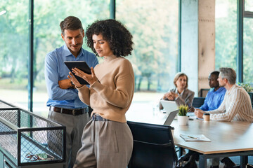 Two business people discussing work together using a tablet in a modern office