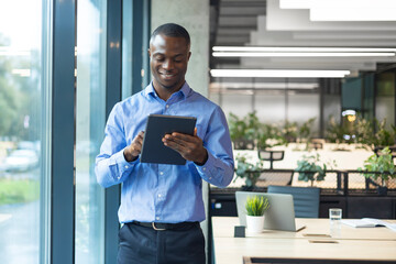 Fototapeta premium Smiling busy african businessman manager using tablet computer standing in office