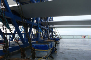 White long blades of wind turbine loaded and lashed by chains and tensioner on the heavy load carrier vessel passing Nord Sea.