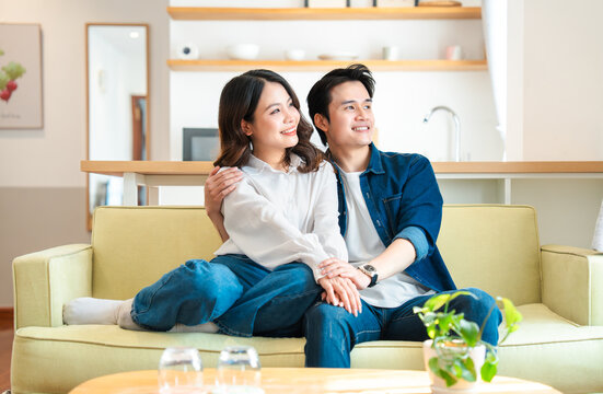 Young couple smiling sitting on a couch looking forward Warm light comfortable and at home - Powered by Adobe