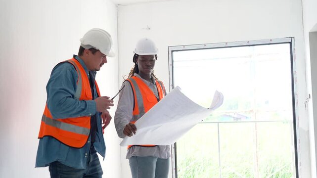group of diversity meeting. construction worker caucasian engineer talking to african american Architects inspection with blue print at Construction site indoors. builder discussion with walkie-talkie