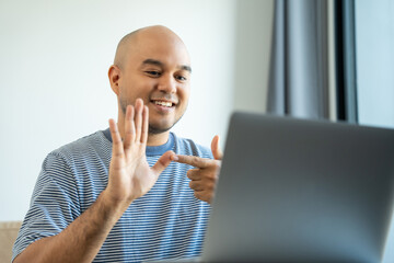 Portrait view of happy young deaf asian man showing sign language and looking at camera at home, a...