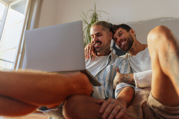 Gay couple watching laptop at home and smiling