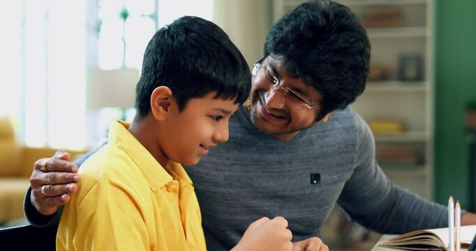 Indian Asian father and young kid celebrating success together at a study table with a laptop, checking results in a modern lavish home, expressing joy and achievement in an educational setting