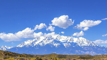 Majestic snowcapped mountain range under clear blue sky with fluffy clouds, showcasing nature beauty and tranquility