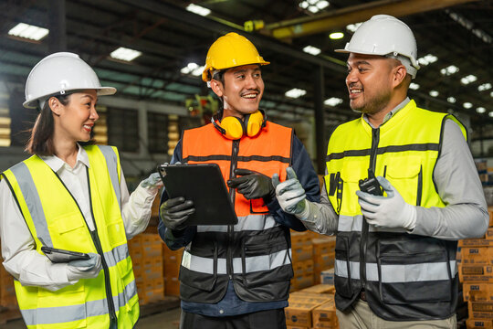 Professional engineer and technician wearing safety helmet analyzing meeting with tablet in factory warehouse. Confident factory workers group inspection industry factory. Teamwork concept.