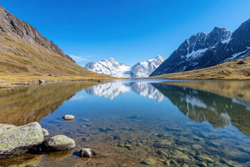 Obraz premium serene mountain lake reflecting majestic snow capped peaks under clear blue sky, surrounded by rugged terrain and tranquil waters