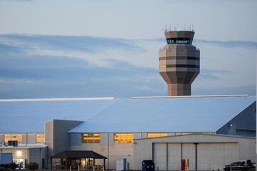 Airport control tower stands above adjacent hangars and service buildings, managing flight operations and airspace activity during dusk at a regional airport