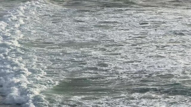 Waves roll towards the shore. White foam on the ocean's surface. Shimmering water reflects soft sunlight. The Atlantic Ocean in Portugal. Magoito beach. Powerful ocean waves. Stormy ocean at sunset.