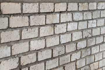 A pale white brick wall is neatly arranged with gray cement layers between the bricks, displaying a rough texture and a repeating rectangular pattern