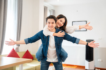Joyful couple having fun together at home woman on man's back arms outstretched smiling widely