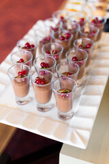 A tray of desserts in small glasses and are topped with berries, ready to be served