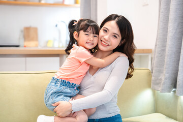 A mother smiling warmly while embracing her young daughter in a cozy living room setting