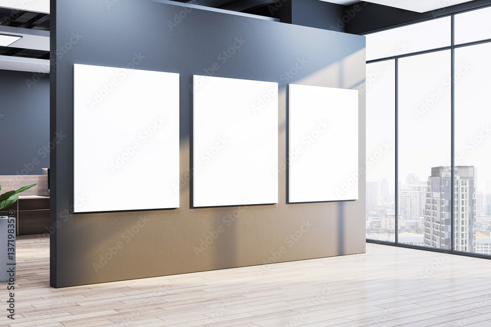 Poster three vertical blank posters on gray wall in modern office interior with large windows and city view